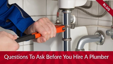 Someone holding an orange wrench by a pipe with banners reading "blog" and "Questions You Must Ask Before You Hire A Plumber"