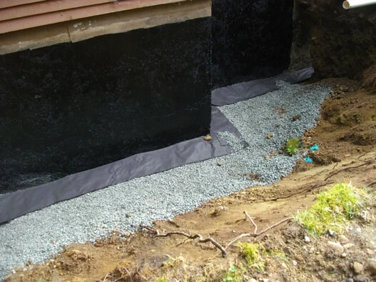 An area near the edge of a home covered in gravel that has been used to fill a hole containing a perimeter drain in Victoria, BC.
