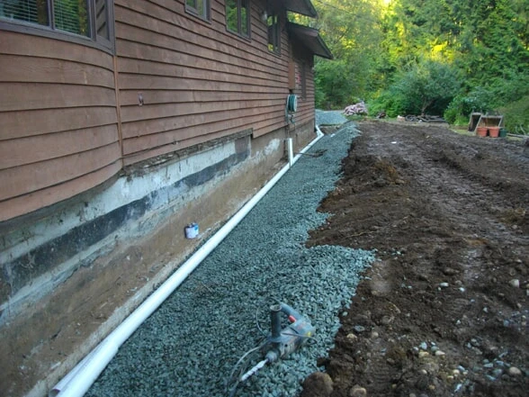 The perimeter of a home with gravel coating the ground after plumbers have dug and installed a perimeter drain in Victoria, BC.
