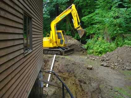 A large piece of machinery being driven and used to dig a perimeter drain in Victoria, BC.