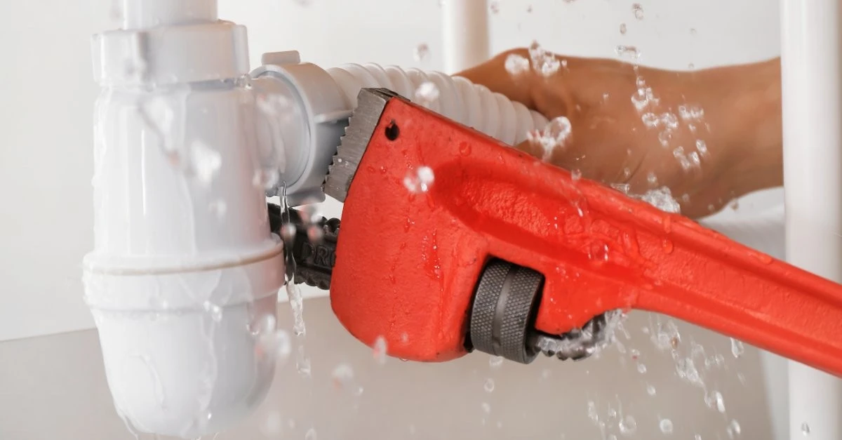  A plumber using a wrench to repair a burst pipe that is actively leaking water.