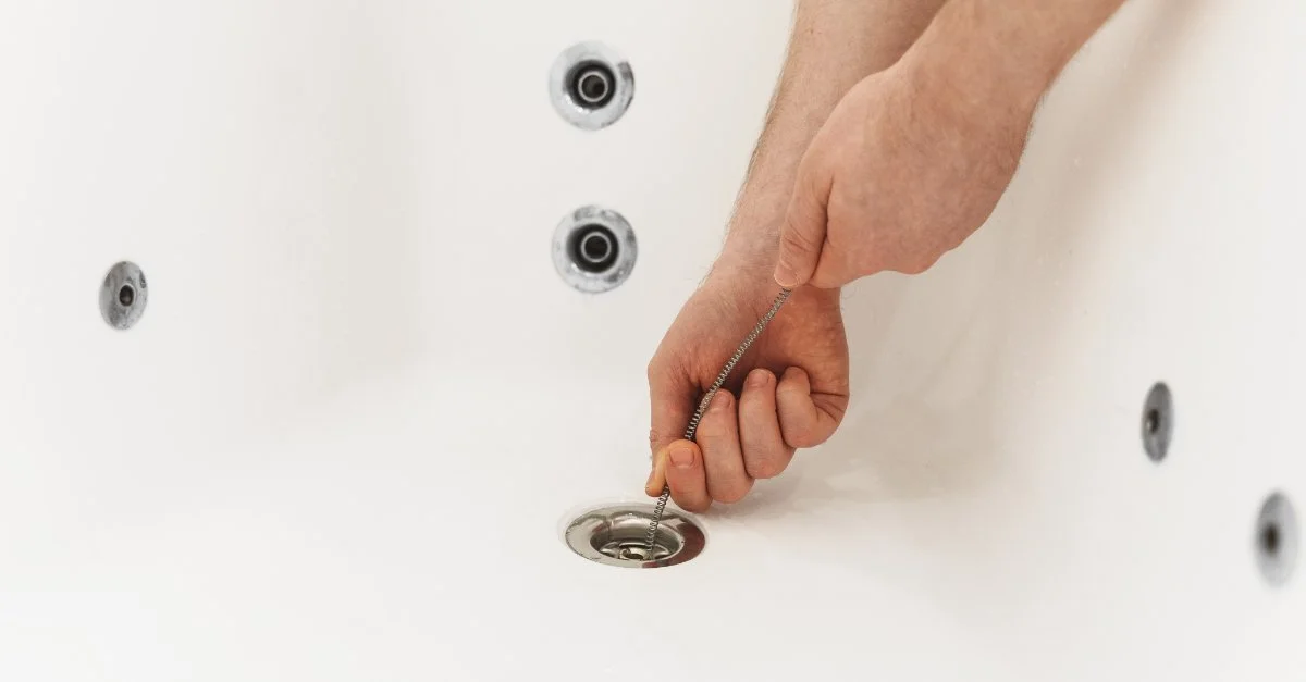 A plumber’s hands as they use a drain snake to clear a bathtub drain during an appointment for drain cleaning in Vancouver, BC.