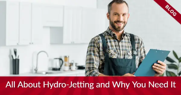 Man in overalls with a clipboard in a kitchen with banners reading "blog" and "all about hydro-jetting and why you need it"