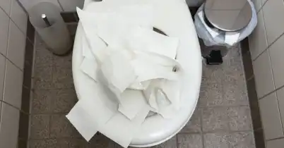 A top-down view of a clogged toilet full of toilet paper in a residential bathroom.