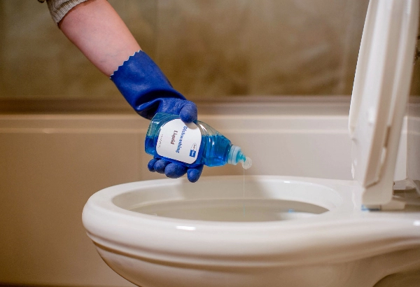 Hand pouring dish soap into a toilet
