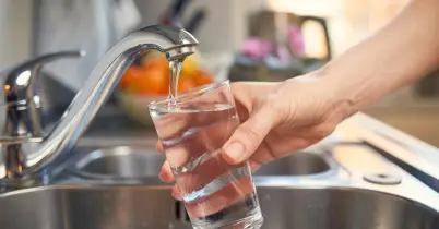 Hand filling up a glass of water from a kitchen faucet.