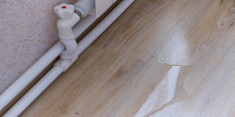 A pipe with a nearby puddle on the floor of a home in need of leak detection in Calgary.