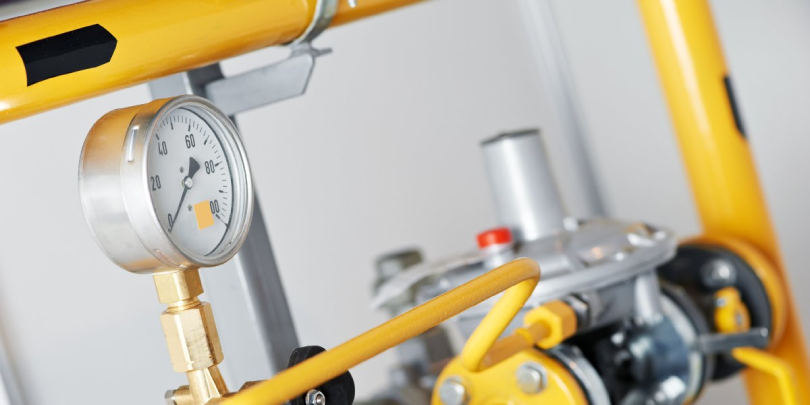 A pressure valve and gauge installed on a yellow pipe attached to a residential plumbing system in Calgary, AB.