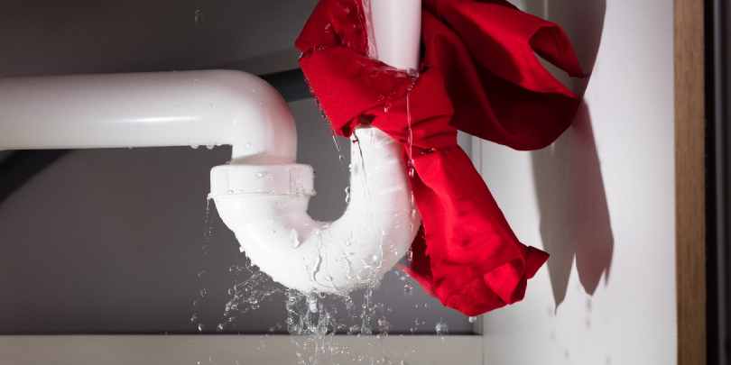 A white, leaking pipe with a red cloth tied around the leaking section to stop the flow of water.
