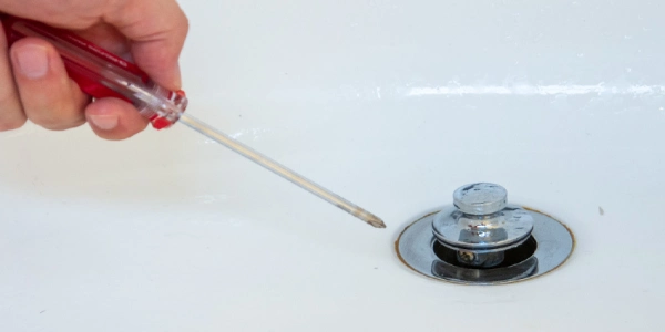 Hand holding a screwdriver to a bathtub drain