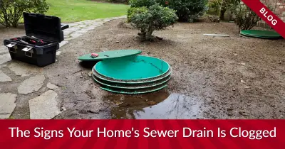 Open sewer drain in yard with text boxes reading "blog" and "the signs your home's sewer drain is clogged"