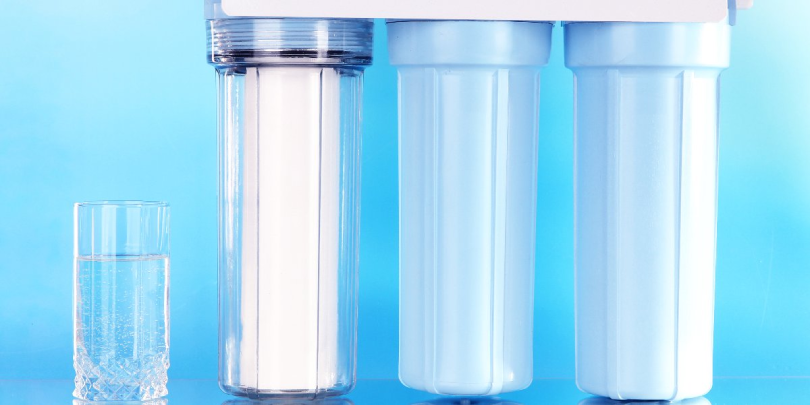 Three filters used for reverse osmosis in Mississauga sitting next to a glass of water.