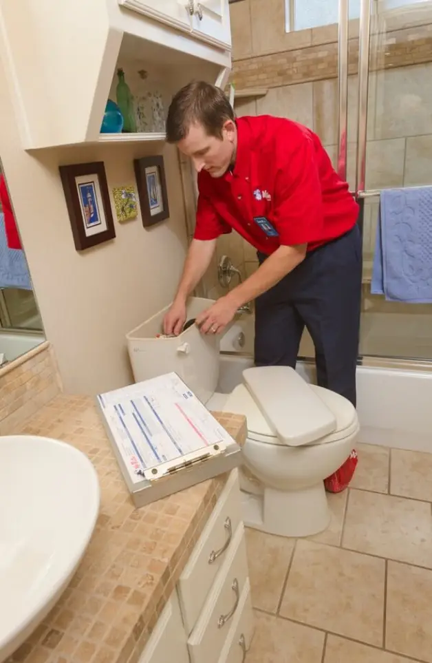 A plumber from Mr. Rooter Plumbing performing repairs inside of a toilet tank in a residential bathroom.