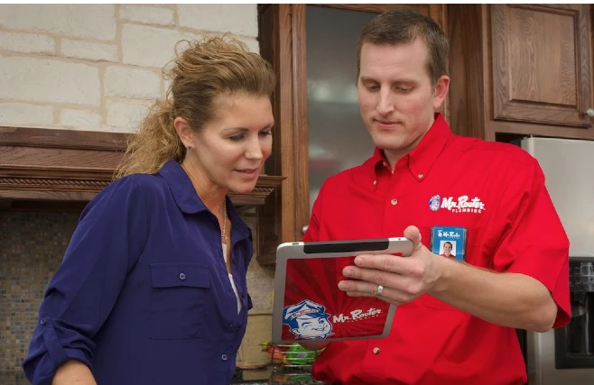A plumber from Mr. Rooter Plumbing using an electric tablet to show a woman her information about plumbing services.