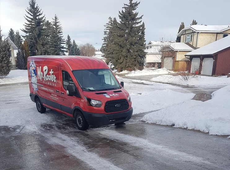 A van branded with the Mr. Rooter Plumbing logo arriving at a home during the winter to provide services for frozen pipe repair.