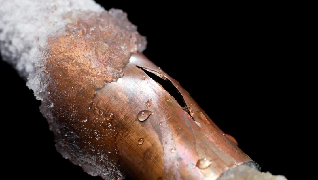 A frozen pipe coated with snow and ice and with a large crack in the side that will require professional service from a plumber familiar with frozen pipes in Mississauga, ON.