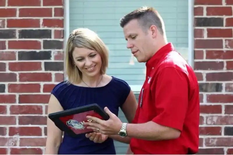 Mr. Rooter plumber with homeowner in front of brick wall, showing homeowner something on a tablet.