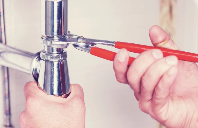 A close-up view of a plumber using a wrench to tighten the connection between two drain pipes during an appointment for drain repair in Ottawa