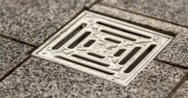 A square, metal drain cover over a drain that has received services for a basement drain backup in Mississauga, ON.