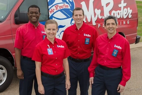 Four smiling plumbers wearing Mr. Rooter Plumbing uniforms and standing in front of a branded van.