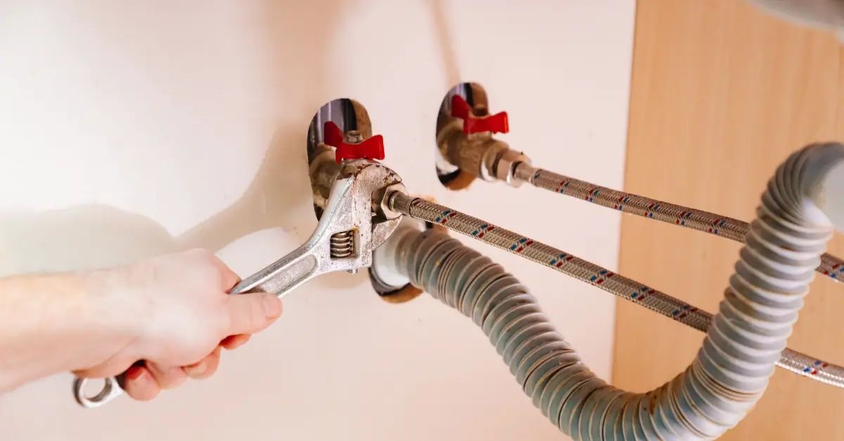 A plumber using a wrench to adjust a faucet on a water heater tank during an appointment for water heater repair in Abbotsford, BC.
