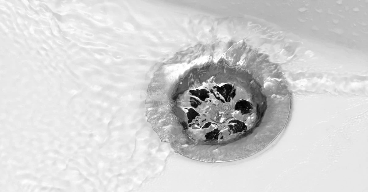 A drain in the bottom of a porcelain sink with free flowing water after it has been cleared with professional service for drain cleaning in Scarborough, ON.