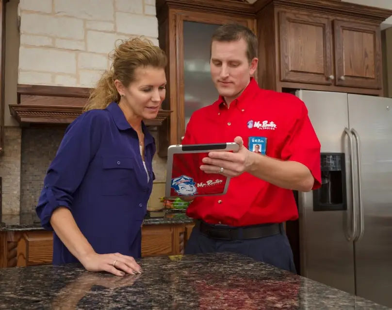  A plumber from Mr. Rooter Plumbing using a tablet to show a homeowner her options for drain cleaning service.
