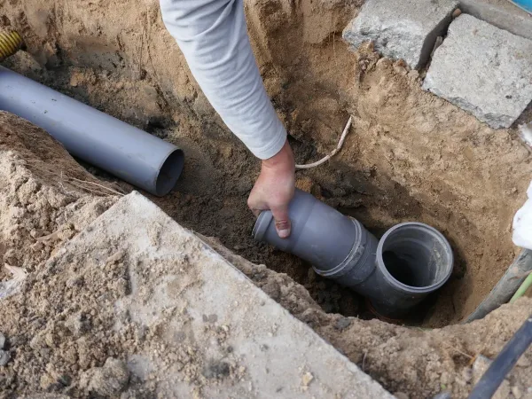 A plumber examining a disconnected sewer line inside of a hole for damage