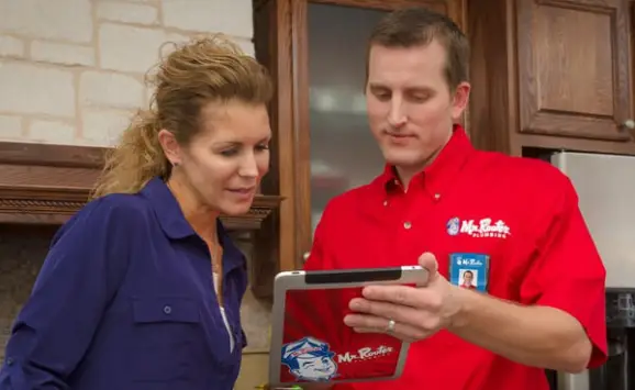 A plumber from Mr. Rooter Plumbing using an electric tablet to show a homeowner information about water line repairs.