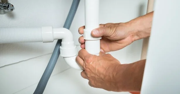 A plumber using their hands to disconnect a P-trap underneath a sink during an appointment to clear clogged drains in Brampton, ON.