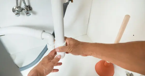 : A plumber using their hands to adjust the connection between the curved section and straight section of a P-trap in the cabinet underneath a sink.
