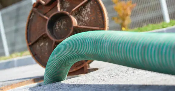 A large green tube going into an open sewer drain cover on a street where sewer cleaning is being completed.