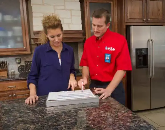 A plumber from Mr. Rooter Plumbing showing a homeowner a clipboard with a sheet containing information about the details and prices of plumbing services.