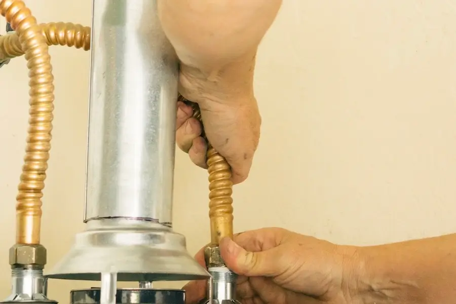 A man’s hands fixing a water line leading into a water heater.