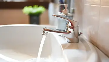 Clean water flowing from a bathroom faucet into the sink and down the drain.