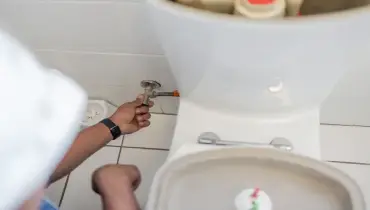 A man shutting off the water supply to the toilet from the shut off valve.