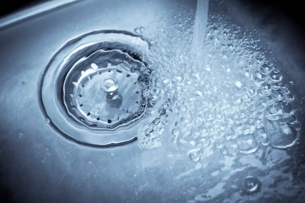 A stainless steel sink full of water with a faucet running.