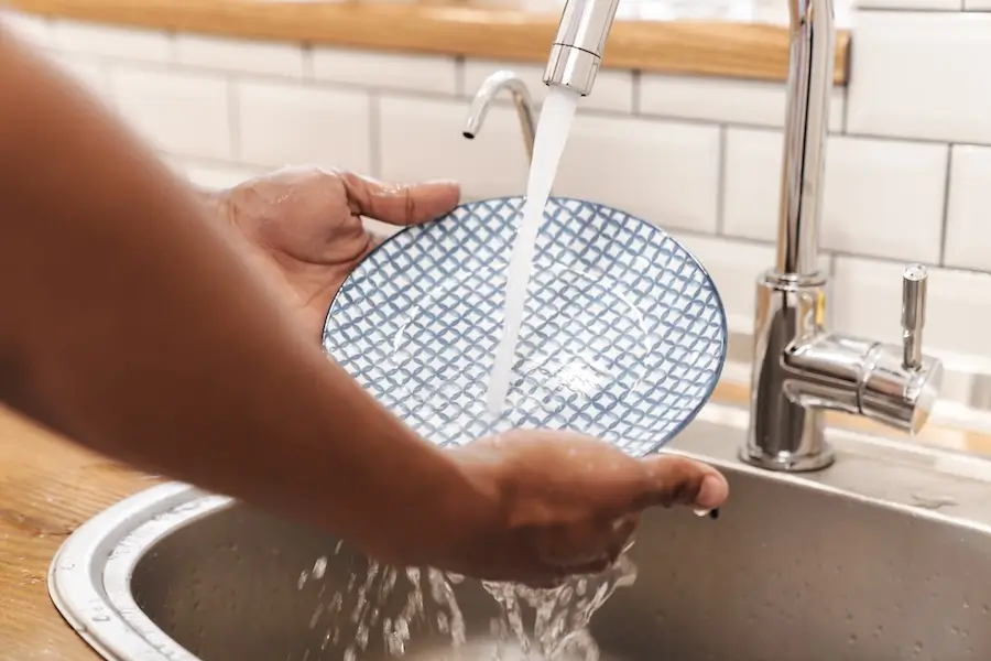 Person washing a blue plate with water at the kitchen sink. 