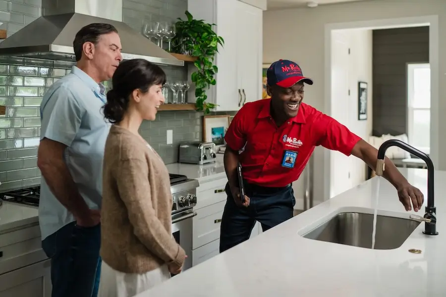 Mr. Rooter Plumbing® professional showing homeowners how he repaired their leaky kitchen faucet.