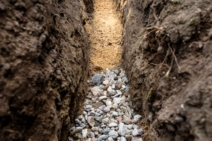 A trench dug for a French drain with yellow soil and gravel.