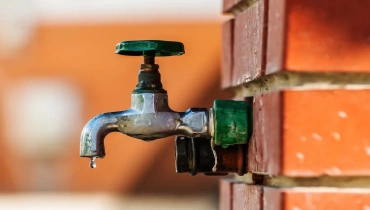 Outdoor faucet against red brick with water dripping from the spout.