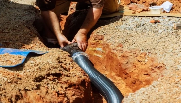 Plumber installing a flexible perforated pipe in a gravel-lined trench for a weeping tile drainage system.