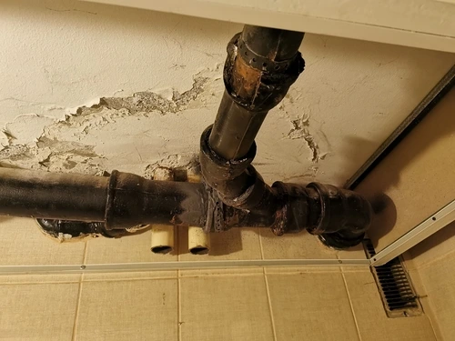 Degraded cast iron pipes against a damaged plaster ceiling