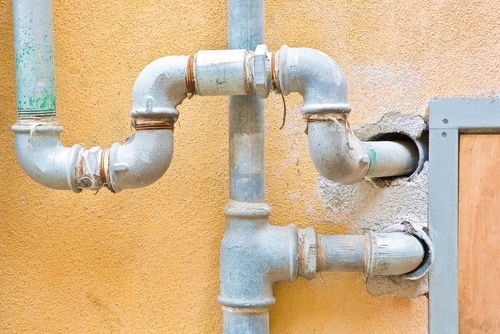 Galvanized steel water pipes running along and into a wall.
