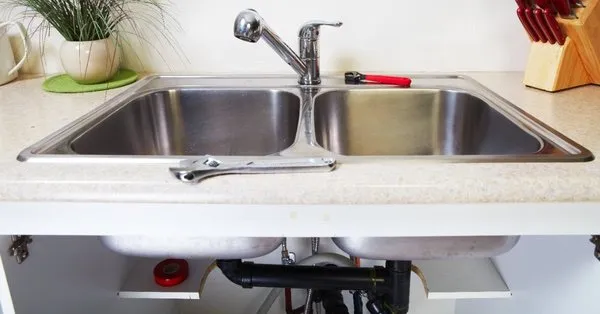 A double kitchen sink with exposed pipes and tools placed nearby for the purpose of drain repair in Newmarket, ON