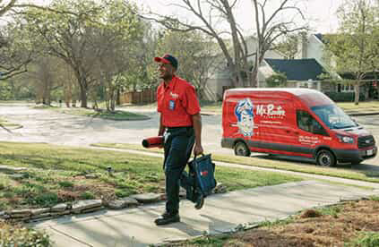 Mr. Rooter service professional walking up sidewalk to client's home with Mr. Rooter van parked behind him on the street.