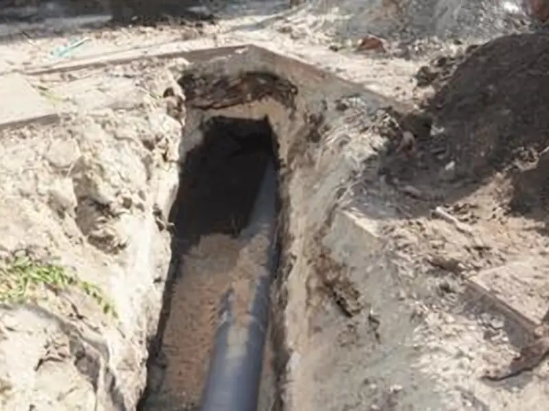 An excavated trench in an Ottawa yard exposing a damaged sewer pipe surrounded by dirt and rubble.