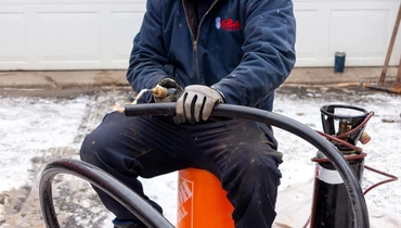 A professional plumber handling sewer equipment outdoors during a repair job in winter conditions.
