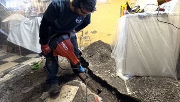 A professional plumber breaking through a concrete floor to access underground plumbing during a repair.