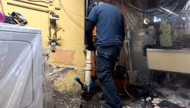 A professional plumber repairing exposed pipes in a residential basement, working on a drainage system.